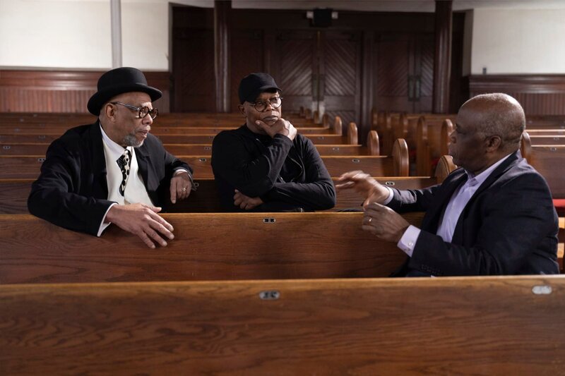 Samuel L. Jackson (M.) spricht mit den Musikern Clark White (l.) und Paul Kwami (r.) über ein altes Sklavenlied, das auf den Baumwollfeldern gesungen wurde. – Bild: (C)HISTORY /​ Associated Producers Ltd.
