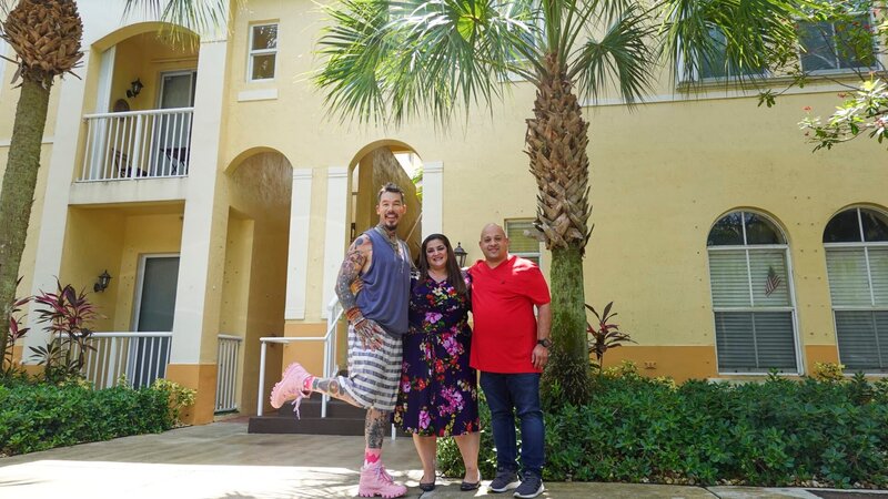 From left to right: Host David Bromstad, Giovanna Lupo, and Giovanni Salazar pose for a picture outside of House 1, Cooper Colony, Hero. – Bild: HGTV US /​ 2023 Warner Bros. Discovery, Inc. or its subsidiaries and affiliates. All rights reserved.