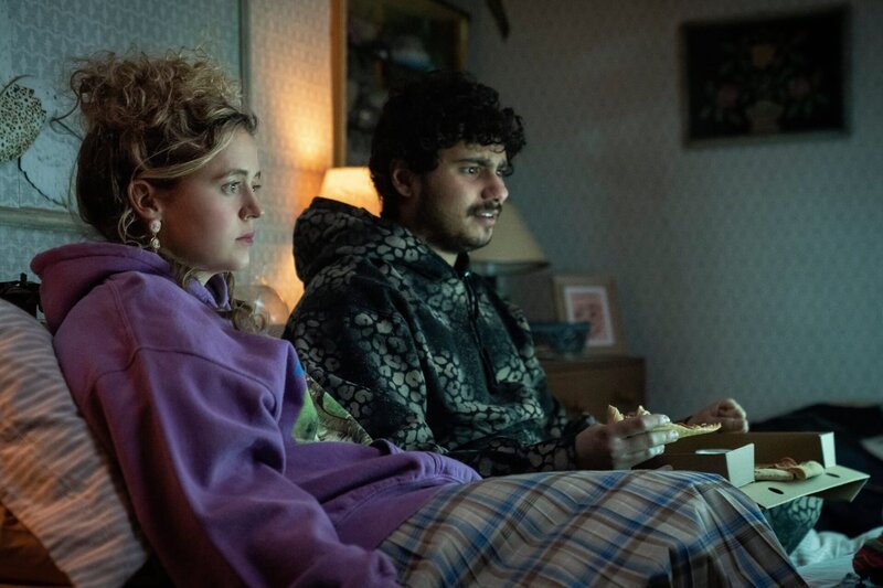 Carrie (Sofia Oxenham, l.) und Kash (Bilal Hasnah, r.) haben ihr Date im Bett. Kash ist froh, dass er mit Carrie zusammen sein kann. Sie liegen im Bett und gucken eine Serie. Kash ist begeistert und albert rum, Carrie dagegen kommt mit der Situation einfach nicht klar. – Bild: Olly Courtney/​Disney+