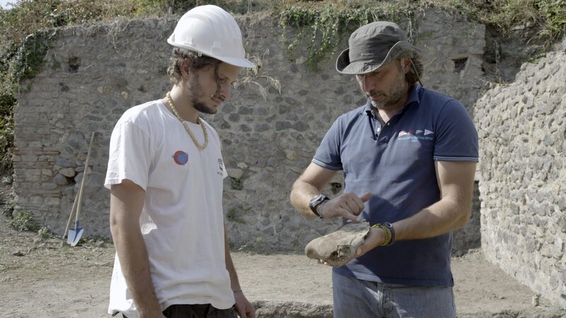 Der Archäologiestudent Dario Lo Surdo (L) und der Archäologe Mario Grimaldi von der Universität „Università degli Studi Suor Orsola Benincasa“ untersuchen einen Ochsenschädel, der unter einer Straße in Pompeji gefunden wurde. (Kredit: National Geographic/​Annamaria Craparotta) – Bild: Disney+