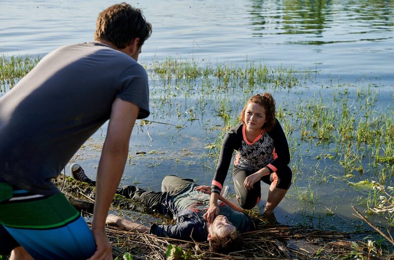 Das morgendliche Stand-up-Paddling von Jakob Frings (Max König, l.) und Julia Demmler (Wendy Güntensperger, r.) in der Liebesbucht findet ein jähes Ende, als Julia einen leblosen Körper am Ufer des Bodensees entdeckt. – Bild: ARD/​Nicolas Gradicsky
