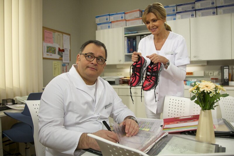 Schwester Yvonne (Maren Gilzer) hat sich neue Jogging-Schuhe gekauft. Pfleger Hans-Peter Brenner (Michael Trischan) ist allerdings wenig angetan – weder von diesem Sport, noch von der Farbe der Schuhe. Als Schwester Yvonne ihm mitteilt, dass auch er ein bisschen Bewegung vertragen könnte, versichert Hans-Peter ihr, dass er sich wohl fühle, genauso wie er ist. – Bild: BR/​MDR/​Rudolf Wernicke