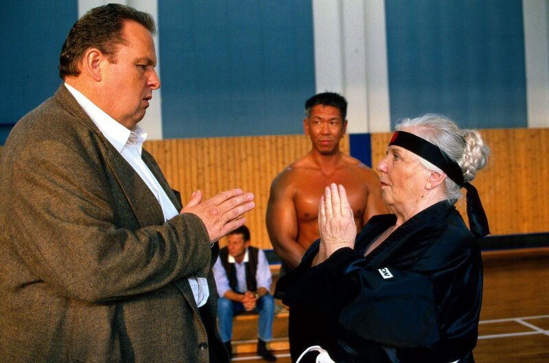 Mutter Resi (Ruth Drexel, r.) hat sich zu einem Selbstverteidigungskurs bei Bruce Adelholzer (Jocky Wong, M.) angemeldet. Stolz zeigt sie Benno (Ottfried Fischer, l.), wie man einen Kampf beginnt. – Bild: Sat.1