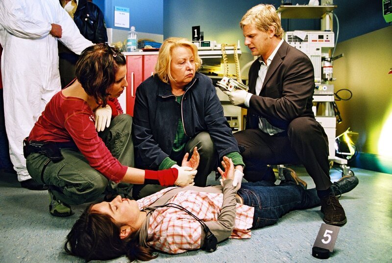Während der Dreharbeiten zu der beliebten Serie „Alpenklinik“ stirbt Lisa (Nicole Uekermann, liegend), als sie ein Elektroschockgerät berührt. Nina (Elena Uhlig, l.), Dr. Reiter (Sarah Camp, M.) und Leo (Henning Baum, r.) untersuchen den Tatort – und tippen auf Mord … – Bild: SAT.1 /​ Christian A. Rieger Eigenproduktionsbild frei