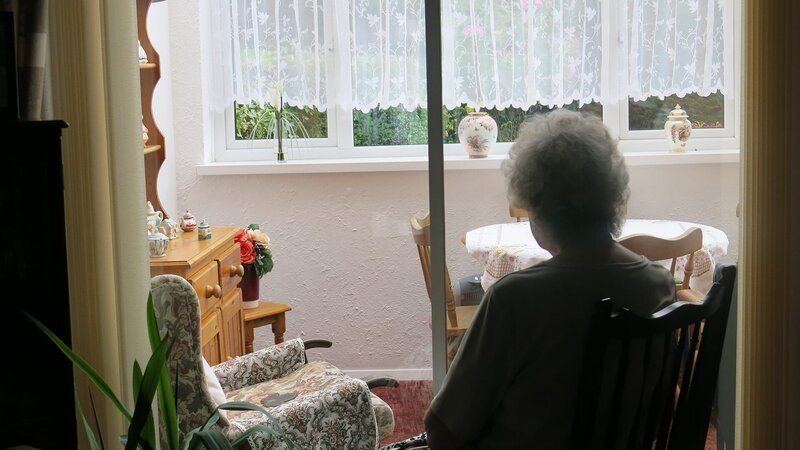Oma schaut aus dem Fenster. – Bild: Flame TV