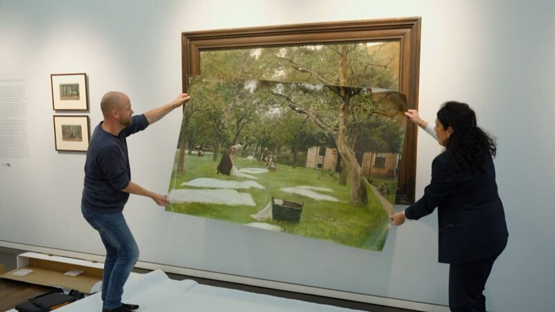 Tim Ernst vergleicht die Reproduktion, die ihm als Vorlage dient mit dem Originalwerk „die Rasenbleiche“ von Max Liebermann. – Bild: Tom Kreyssig