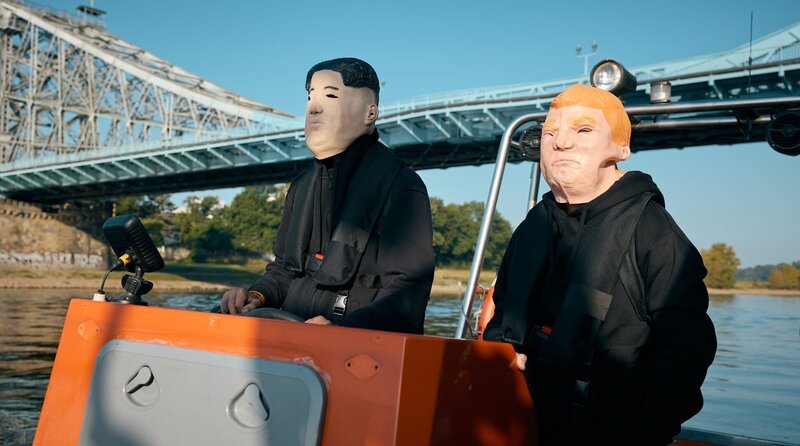 Zwei maskierte Personen, jeweils als Trump und Kim Jong Un fahren mit einem Motorboot. – Bild: Rudolf Wernicke