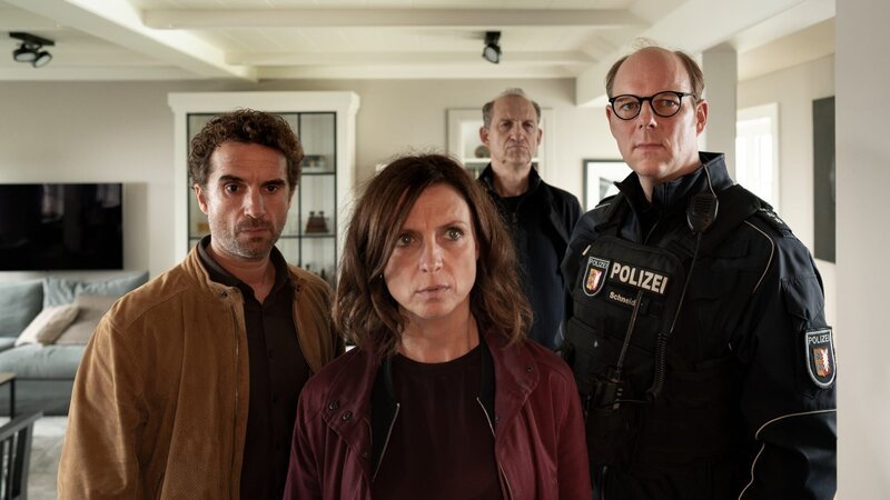 Durch Zufall findet Polizist Schneider (Stephan A. Tölle, r.) in einem Schrank die Bogenschießausrüstung von Leif Conradi. Hinnerk Feldmann (Oliver Wnuk, l.), Ina Behrendsen (Julia Brendler) und Carl Sievers (Peter Heinrich Brix, 2.v.r.) rätseln, ob der Autor mit seinem eigenen Equipment getötet wurde. – Bild: Georges Pauly