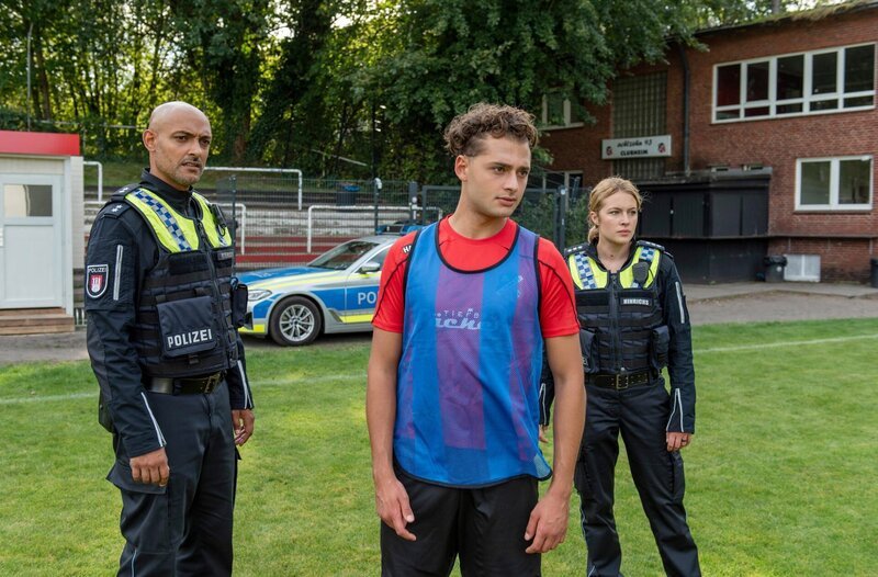 Ein Mitspieler kommt bewusstlos ins Krankenhaus, nachdem er aus der Trinkflasche von Matthias Kemper (Samy Abdel Fattah, M.) getrunken hat. Galt der Anschlag eigentlich ihm? Lukas Petersen (Patrick Abozen, l.) und Bente Hinrichs (Sinha Melina Gierke, r.) gehen dieser Frage nach. – Bild: ARD/​Thorsten Jander
