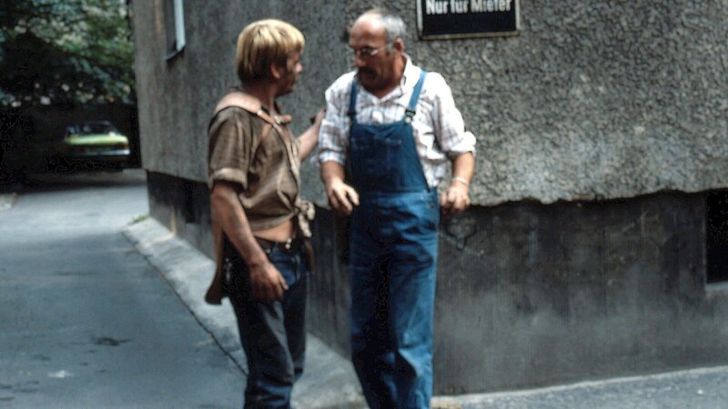 Peter Lustig (r.) ist über einem Kohlestückchen auf dem Bürgersteig ausgerutscht. Irritiert und verwundert über die herumliegende Kohle, spricht er den „Kohlemann“(l.) an. Dieser hat aber nur wenig Verständnis für Peters Fragerei. – Bild: ZDF und Studio-TV