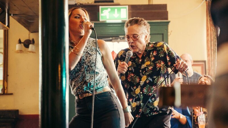 Während alle anderen mit der Suche nach ihrem Freund beschäftigt sind, bleibt Frank (Christopher Walken) zurück. Eines führt zum anderen und schon findet sich Frank beim Karaoke in einer Bar wieder. – Bild: ZDF und James Pardon./​James Pardon