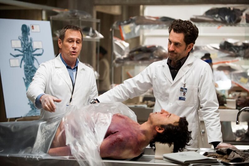 Die Leiche von Joel Summers (Jason Blicker, liegend) ist eine von 17, die zu einer grausamen Skulptur geformt wurden. Brian Zeller (Aaron Abrams, r.) und Jimmy Price (Scott Thompson, l.) untersuchen die sterblichen Überreste genau … – Bild: NBCUniversal Media, LLC /​ Brooke Palmer