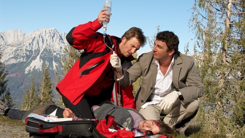 Hans (Heiko Ruprecht, l.) und Bergdoktor Martin (Hans Sigl, r.) versorgen die schwer verletzte Tanja Grünert (Karin Thaler) an der Unfallstelle. – Bild: Walter Wehner