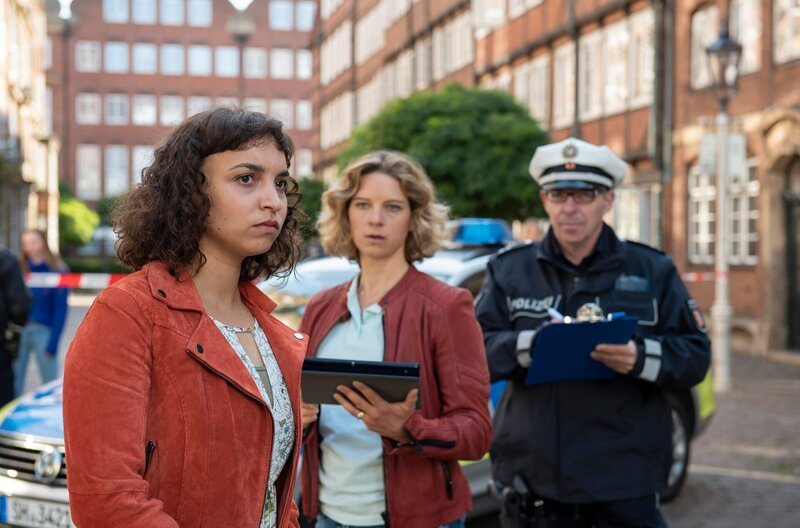 Aufgewühlt schildert Gesa Frahm (Genet Zegay, l.) Kommissarin Tomke Jennsen (Anjorka Strechel, M.) und einem Polizeibeamten (Komparse, r.) den Unfallhergang. – Bild: ARD/​Thorsten Jander