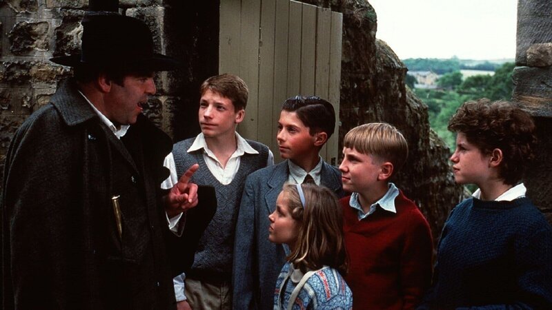 Die Kinder Julian (Marco Williamson, 2.v.l.), Pete (Ian Aherne, 3.v.l.), Dick (Paul Child, 2.v.r.), George (Jemima Rooper, r.) und Anne (Laura Petela, 3.v.r.) begegnen dem mysteriösen Barling (Jeremy Sinden, l.), der sich als Experte für Vögel ausgibt. Doch die Gruppe ist skeptisch und lässt sich von seiner Geschichte nicht täuschen. – Bild: Moira Conway