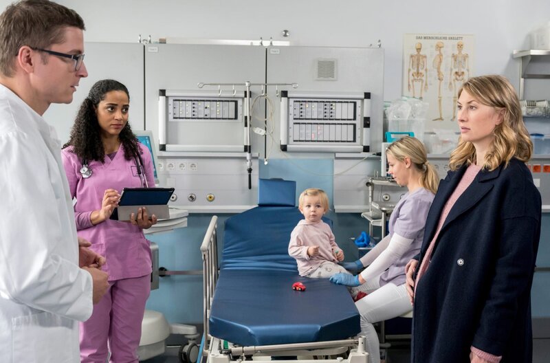 Dr. Elias Bähr (Stefan Ruppe, l.) betreut mit Dr. Emma Jahn (Elisa Agbaglah, 2.v.l.) die hochschwangere Tanja Jakobs (Gabriela Lindl, r.), deren eineinhalb-jährige Tochter Lotte operiert werden muss (mit Komparsin). – Bild: ARD/​Jens Ulrich Koch