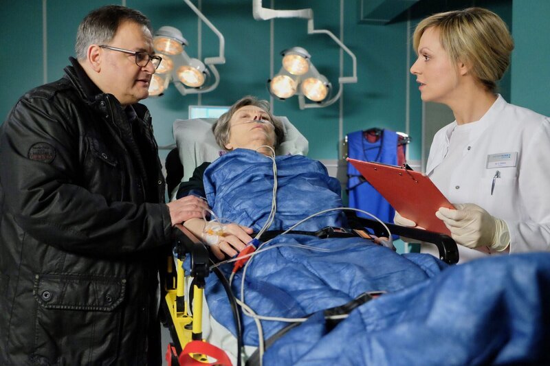 Hans-Peter Brenners (Michael Trischan, links) Mutter Luise (Monika Lennartz, Mitte) ist zusammengebrochen. Während der Untersuchung durch Dr. Lea Peters (Anja Nejarri, rechts) weicht er nicht von ihrer Seite, was Leas Arbeit nicht leichter macht. – Bild: BR/​MDR/​Saxonia Media Filmproduktions GmbH /​ Sebastian Kiss