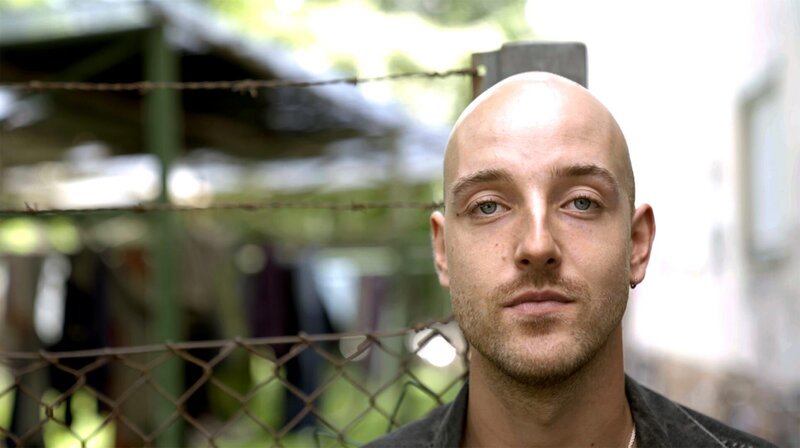 Philip, 27,  Designstudent und Fotograf. Wird von André eingeladen, im OMZ als „Artist in Residence“ zu leben. Ist sehr bald nicht nur Chronist, sondern auch Ansprechpartner für die Bewohner, Vermittler bei Streits, Leiter des Plenums. – Bild: SWR