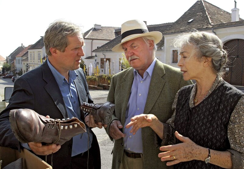 Thomas (Harald Krassnitzer, links) zeigt seiner Mutter (Christine Ostermayer) und Gottfried Schnell (Wolfgang Hübsch) die Pferdeleder-Schuhe, die er beim Entrümpeln des Nachlasses seines Vaters gefunden hat. – Bild: BR/​ARD/​ORF/​Petro Domenigg