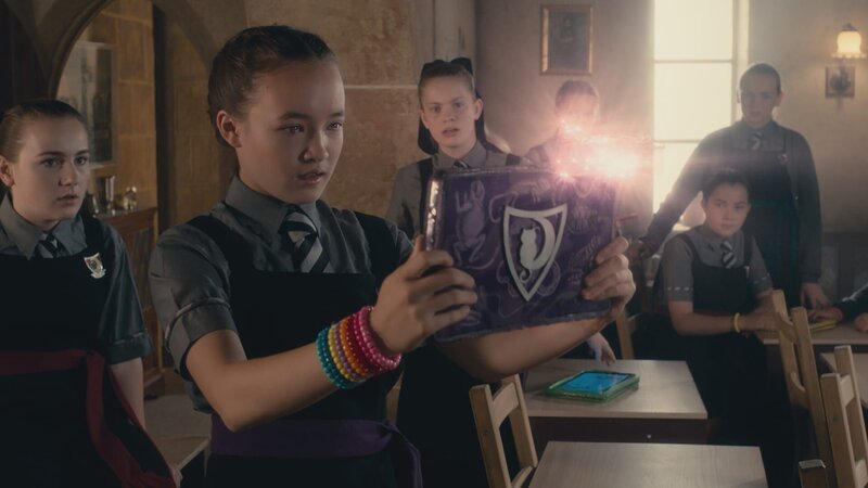 Esther (Jenny Richardson, 3.v.l.) und andere Mitschülerinnen beobachten Felicitas (Dagny Rollins, 2.v.l.), die wie süchtig das neue Spiel auf ihrem Maglet spielt. – Bild: ZDF/​CBBC/​ZDF Enterprises 2019 /​ KiKA Bildredaktion