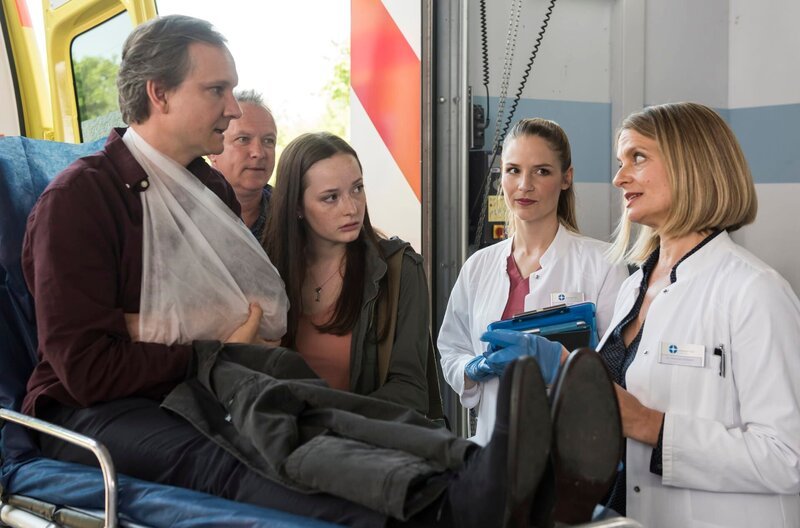 Olaf Schönholz (Sebastian Weber, l.) wird mit einem Schlüsselbeinbruch ins JTK eingeliefert. Seine Tochter Jeanette (Johanna Werner, 2.v.l.) ist den Ärzten gegenüber skeptisch. Julia Berger (Mirka Pigulla, 2.v.r.) und Dr. Franziska Ruhland (Gunda Ebert, r.) gehen von einem Routinefall aus. – Bild: ARD/​Jens Ulrich Koch