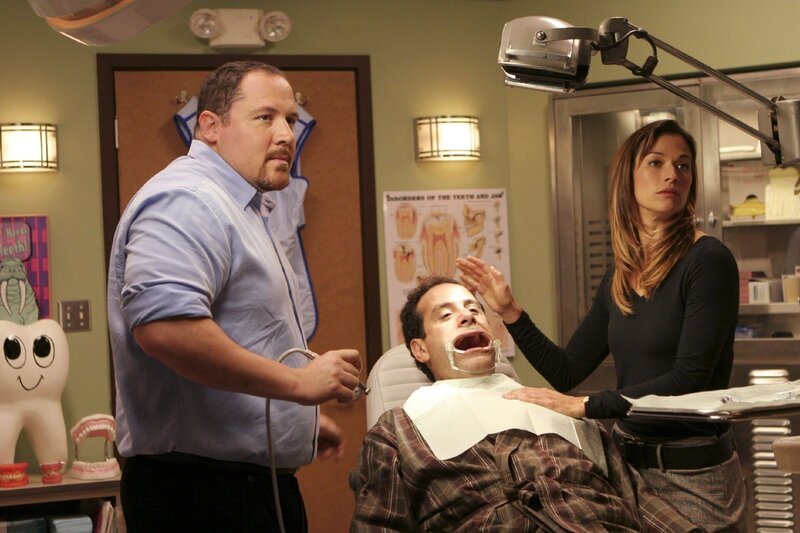 Dr. Bloom (Jon Favreau, l.) lässt Monk (Tony Shalhoub) von seiner Assistentin Terri (Brooke Langton) entführen und bindet ihn auf seinem Behandlungsstuhl fest, um mit Bohrer und Zange herauszufinden, was Monk bereits über ihn weiß … – Bild: RTL