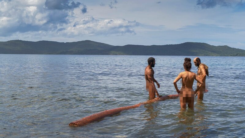 Survivalisten ziehen Baumstämme aus dem Wasser. – Bild: Warner Bros. Discovery