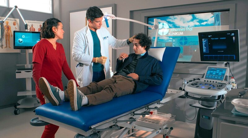 Mit einem Verdacht auf ein Schädel-Hirn-Trauma wird Enzo Falcone (Béla Can Leon, r.) von Rebecca (Milena Straube, l.) und Ben (Philipp Danne, M.) untersucht. – Bild: ARD/​Saxonia Media