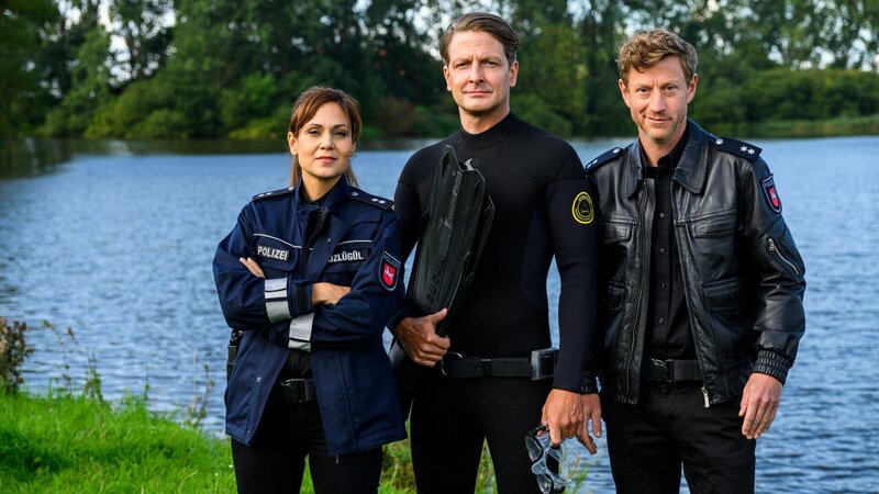 Süher Özlügül (Sophie Dal, l.) und Henk Cassens (Maxim Mehmet, r.) sind dabei, als Bestatter Wolfgang Habedank (Holger Stockhaus, M.) bei seinem neuesten Hobby, dem Apnoetauchen, eine Leiche in der Ems entdeckt. – Bild: ZDF