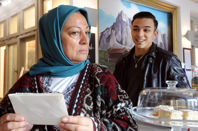 Sevim (Özay Aslanhan) blickt nachdenklich vom Brief ihrer Tochter hoch, als Leon (Joel Akgün) freudig ins Kiosk kommt. – Bild: Marco Orlando Pichler /​ BR