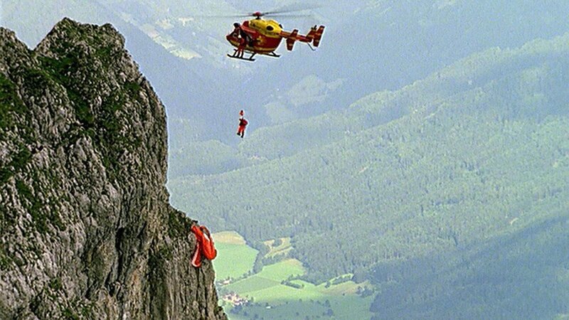 Sybill Regner (Claudia Ziegler) ist beim Paragleiten gegen eine Felsvorsprung geprallt und hängengeblieben. Um die Verunglückte zu bergen, muss sich Dr. Lüdwitz (Rainer Grenkowitz) vom Medicopter aus in die Tiefe abseilen. Windböen erschweren die Bergung zusätzlich. – Bild: SUPER RTL