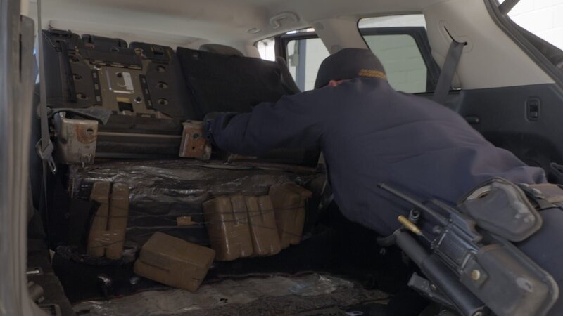 Ein CBP-Beamter holt Pakete mit mutmaßlichen Betäubungsmitteln heraus, die unter dem Rücksitz des Fahrzeugs eines Verdächtigen in Hidalgo, Texas, gefunden wurden. (National Geographic) – Bild: Disney