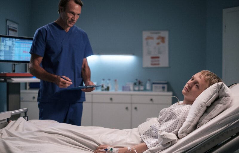 Dr. Martin Stein (Bernhard Bettermann, li.) hat Jan Winkler (Jakob Schmidt, re.) einen Tumor an der Wirbelsäule entfernt. Doch statt der Besserung kann Jakob nach der OP seine Beine gar nicht mehr bewegen. – Bild: MDR/​Saxonia media/​Robert Strehler