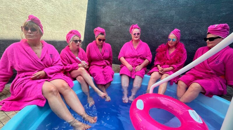 Schillernde Runde und drei Generationen zusammen im Spa – in pink und Frottee: Wegbegleiterinnen wie Gayle Tufts, Daphne de Luxe, Katie Freudenschuss, Julia Gamez Martin und Miss Allie beschreiben, welche Pionierarbeit Gerburg Jahnke für Frauen im Comedy-Bereich geleistet hat. – v.l.n.r. Katie Freudenschuss, Miss Allie, Julia Gámes Martin, Daphne de Luxe, Gerburg Jahnke, Gayle Tufts – Bild: WDR/​Claus Schmitz