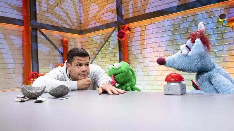 Woozle (re.) hat das Ei einer kuscheligen Woozlinger Flausch-Echse mit ins Studio gebracht, aber Simón (li.) ist skeptisch. Und tatsächlich: Woozle brütet stattdessen aus Versehen ein beängstigendes Chawoozleon (mi.) aus, das gleich darauf auch noch verschwindet! Ob die beiden es einfangen können, bevor es das ganze Studio verwüstet? – Bild: Annette Etges/​SUPER RTL