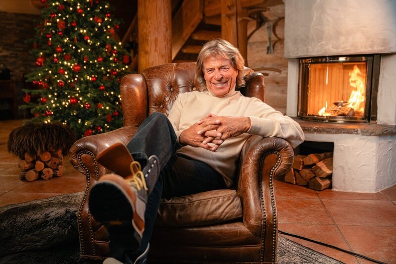 Hansi Hinterseer in einer gemütlichen Weihnachtlichen Stube vor Kaminfeuer während der Dreharbeiten für die Sendung „Weihnachtslichter“ – Bild: ServusTV /​ Moonlake Entertainment /​ Markus Christ