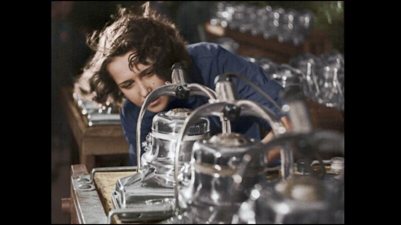 Frau im blauen Arbeitshemd steht hinter einem Maschinenteil für einen Staubsauger. – Bild: RTL /​ © Azor Producciones /​ British Pathé