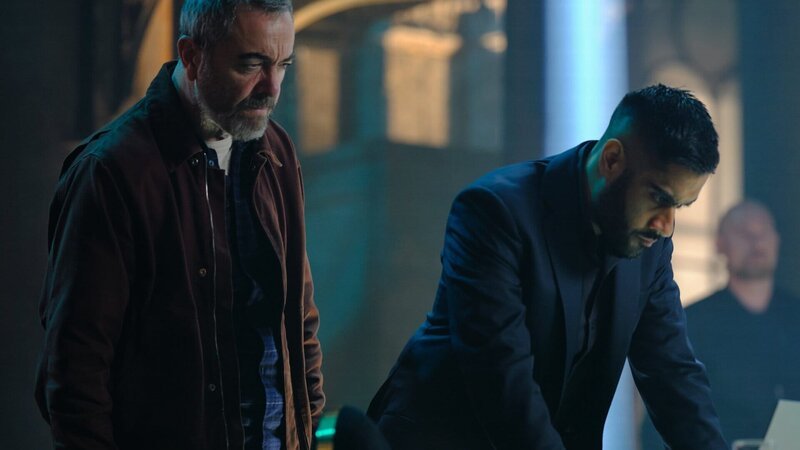 Jaisal (Sacha Dhawan, r.) bietet Danny (James Nesbitt, l.) an, ihm die Bilder seiner Überwachungskameras zu zeigen. – Bild: ZDF und LAURENCE CENDROWICZ
