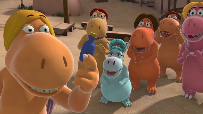 Der neue Fitnesstrainer Sebastian steht umringt von sämtlichen Frauen der Dracheninsel und hält ein kleines blaues Fläschchen in die Höhe. – Bild: ZDF/​Caligari Film