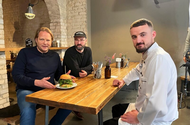 In Münster probiert Björn Freitag (l.) bei Restaurantbereiber Mike Gottlob (m.) und Koch Gentian Koçi (r.) eine Fusion-Burger-Kreation. – Bild: WDR/​solisTV/​Joshua Stolz