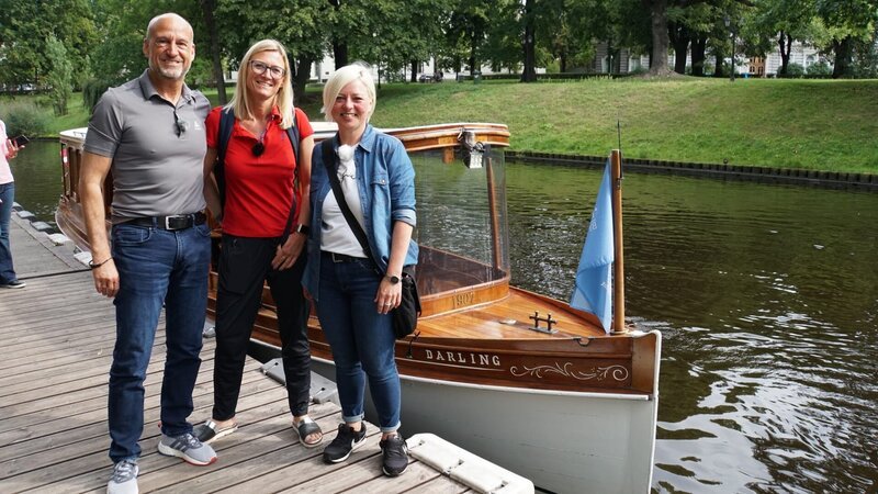 Die „Grand Lady“ in Riga in Lettland. Ausflug: Kanalfahrt und Marktbesuch mit den Passagieren Sandra und Michael Fuhr. Guide Kirsten wartet schon auf Captain Janis an der kleinen Anlegestelle gegenüber des Kreuzfahrtterminals mit einem kleinen Holzboot. – Bild: Deborah Stöckle /​ BR, Bewegte Zeiten Filmproduktion GmbH