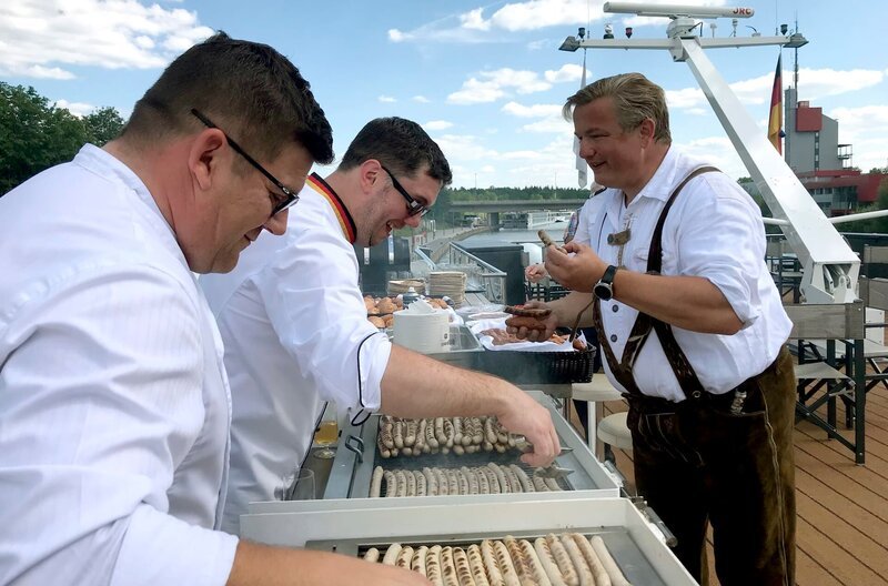 Marcus Kirchgäßner grillt auf dem Sonnendeck Würste. Rudi van der Meulen probiert diese. – Bild: BR/​Bewegte Zeiten Filmproduktion/​Conny Schulze