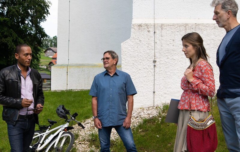 Jerry (Peter Marton, l.) befragt die Sänger am Klosterparkplatz. Dabei fällt ihm auf, wie nervös Laura (Sarah Beck, 2.v.r.) ist (mit Rufus Beck, r. und Komparse, M.). – Bild: ARD/​Lucky Bird Pictures/​Thomas Neumeier