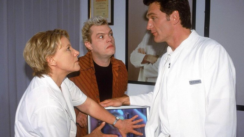 Nikola (Mariele Millowitsch) und Tim (Oliver Reinhard, Mi.) können nicht verhindern, dass Dr. Schmidt (Walter Sittler) die DVD mit dem peinlichen Striptease in den Rekorder legt … – Bild: RTL /​ Guido Engels