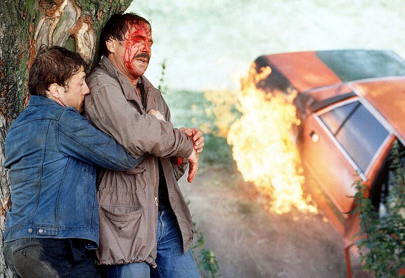 Aus Gründen, die sich Schimanski (Götz George) nicht erklären kann, hat Mandel (Christoph Waltz) ihn aus dem brennenden Wagen gerettet. – Bild: DMB /​ Credit: WDR/​Michael Bshme, Source: WDR-Pressestelle/​Bildredaktion