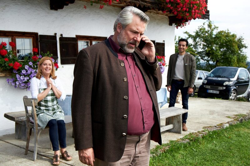 Kommissar Stadler (Dieter Fischer, M.) kann nicht glauben, dass seine Frau Hilde nicht nur seinen Urlaub, sondern auch seine Vertretung, Kommissar Kilian Kaya (Baran Hêvî, r.) aus Passau, organisiert hat. Offenbar freuen sich Marie (Karin Thaler, l.) und Kilian Kaya mehr für die Stadlers als der Kommissar selbst. – Bild: Bojan Ritan /​ ZDF Enterprises GmbH