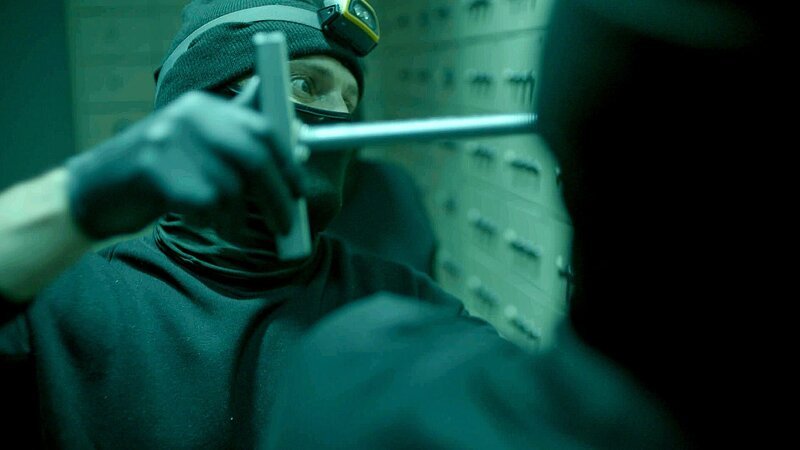 Einbrecher, der ein Bankschließfach mit einem Werkzeug öffnet. – Bild: Warner Bros. Discovery