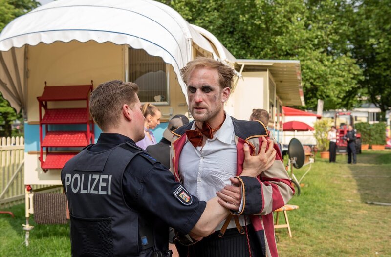 Clown Nils (Maik Rogge) ist völlig aufgelöst, als er von Maschas Tod erfährt, die sich erst vor kurzem von ihm getrennt hatte. Ein uniformierter Polizist hält ihn auf. – Bild: ARD/​Thorsten Jander