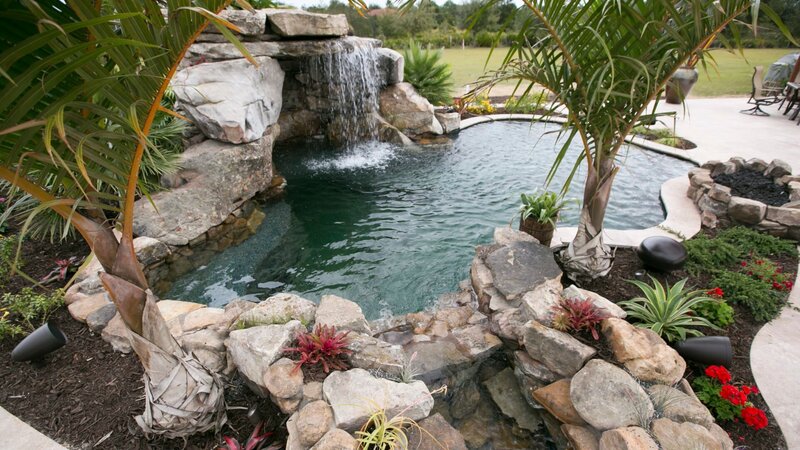 The completed pool area in the backyard of a property with a waterfall, garden and entertainment area. – Bild: Discovery Communications