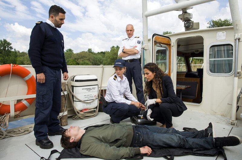 Jasmin Sayed (Sesede Terziyan, r.), Paula Sprenger (Sarina Radomski, 2.v.r.), Wolf Malletzke (Christoph Grunert, im HG) und Fahri Celik (Hassan Akkouch, l.) nehmen die Leiche aus dem Wannsee in Augenschein. – Bild: ARD/​Daniela Incoronato